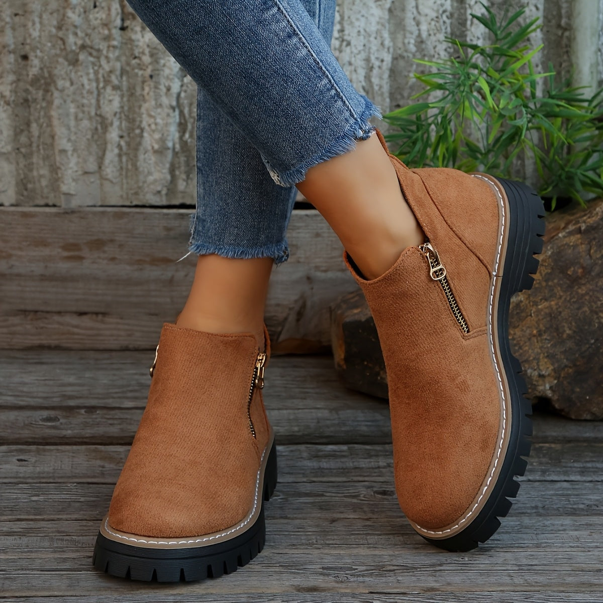 Botines marrones de caña baja con cremalleras laterales, vistos puestos con vaqueros junto a un entorno exterior rústico.