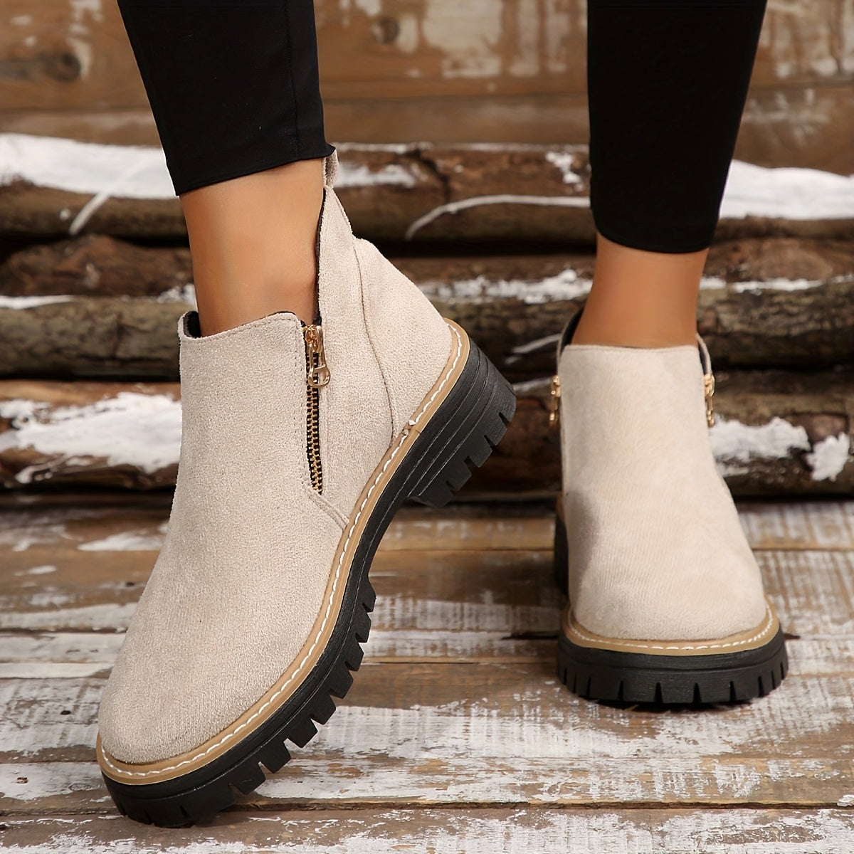 Botines color crema con cremalleras laterales y suelas marcadas, llevados con pantalones negros sobre una escalera de madera.