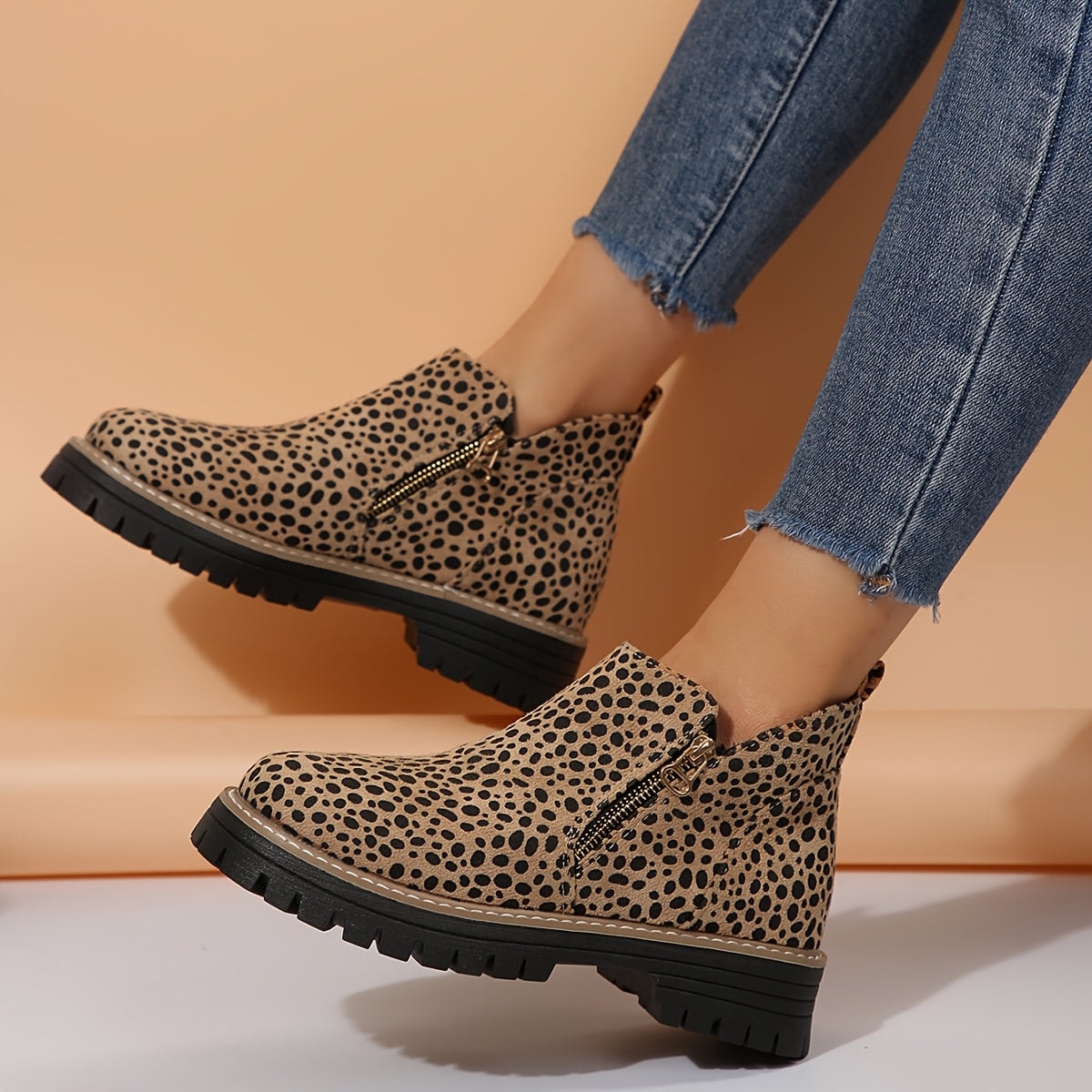 Vista lateral de los botines de estampado de leopardo mientras se llevan con vaqueros, destacando sus cremalleras laterales y suela marcada.