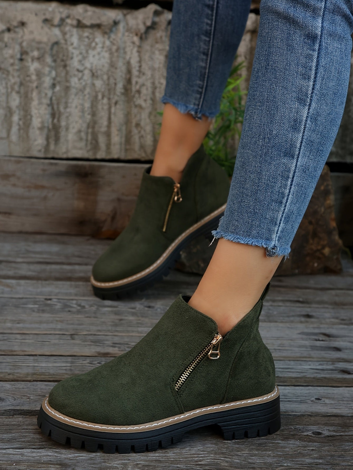 Botines verdes de caña baja con cremalleras laterales, llevados con vaqueros sobre una superficie de madera exterior.
