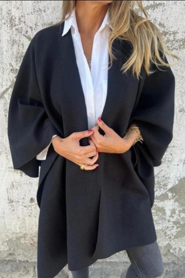 Capa negra abierta de corte amplio sobre una camisa blanca, con mangas anchas y el frente sujetado a la altura del torso.