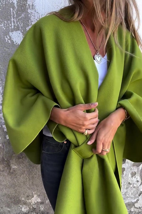 Capa verde oliva de corte amplio, recogida al frente y combinada con una camiseta blanca y vaqueros oscuros.