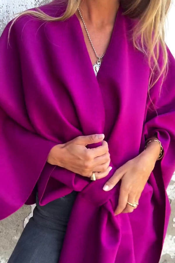 Capa fucsia de caída amplia, con el frente recogido a la altura de la cintura y una manga extendida.