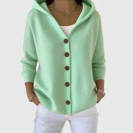 Cárdigan verde menta con capucha, mangas largas y cierre frontal de botones marrones, combinado con pantalón blanco.