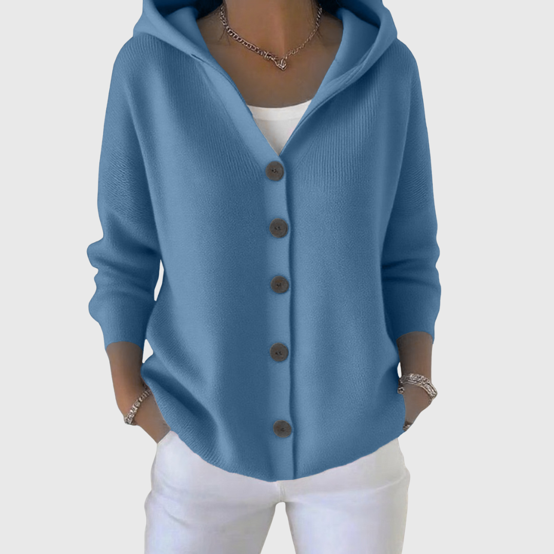 Cárdigan azul con capucha y cierre frontal de botones, llevado con pantalón blanco.
