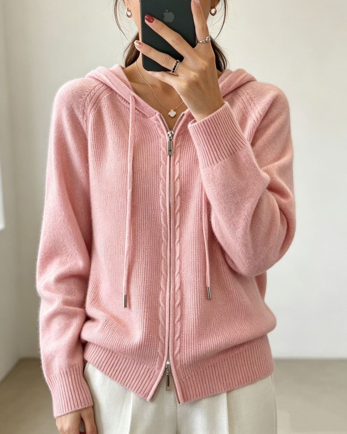 Cárdigan rosa claro con capucha y cordones, cremallera frontal cerrada y detalle trenzado junto al cierre.