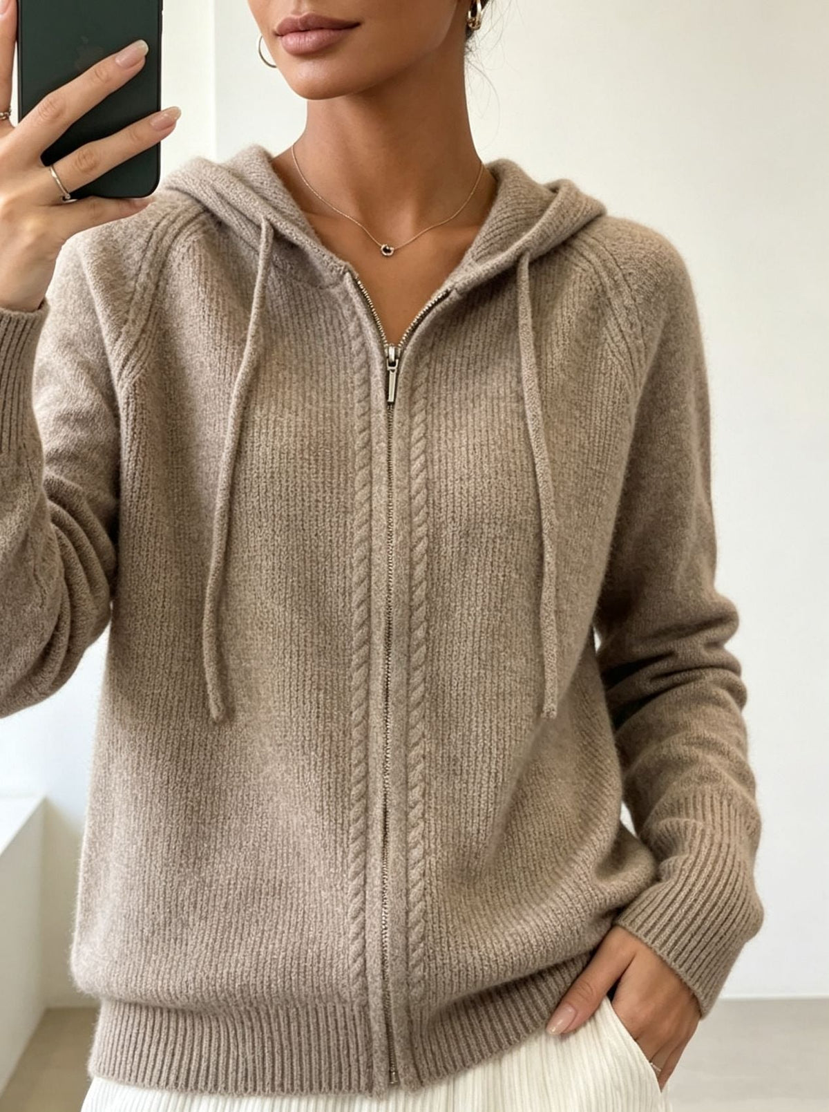 Cárdigan beige con capucha y cordones, cremallera frontal cerrada y bajo acanalado marcado.