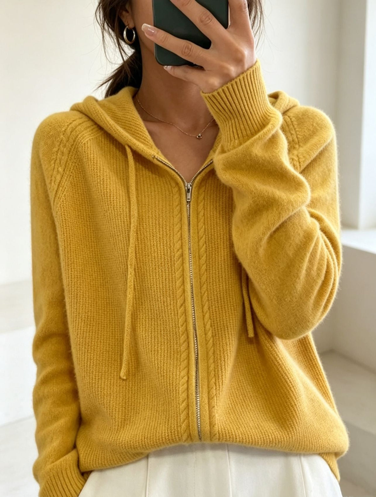 Cárdigan amarillo mostaza con capucha, cordones frontales y cremallera cerrada hasta el bajo.