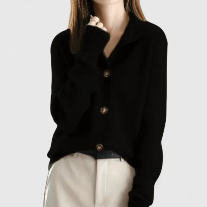 Cárdigan negro de cuello abierto y tres botones visibles, combinado con pantalón de tono claro.