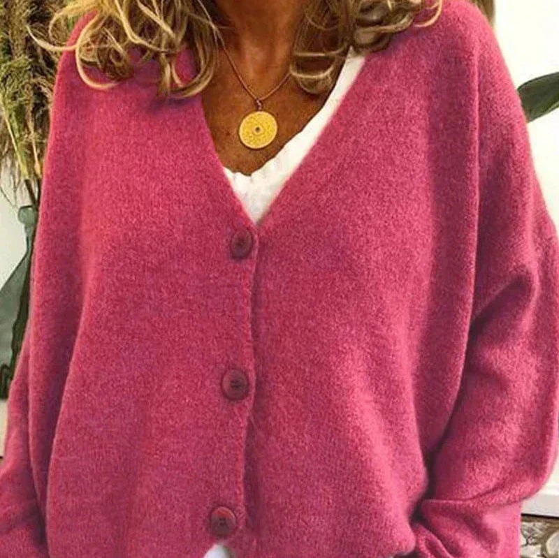 Cárdigan rosa fucsia con tres botones visibles, mangas largas y parte inferior ligeramente ondulada.