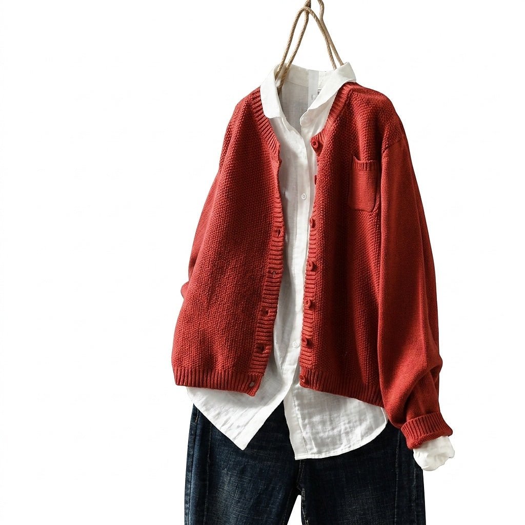 Cárdigan oversize rojo con escote en V, botones frontales y bolsillo en el pecho, combinado abierto sobre una camisa blanca y vaqueros oscuros.