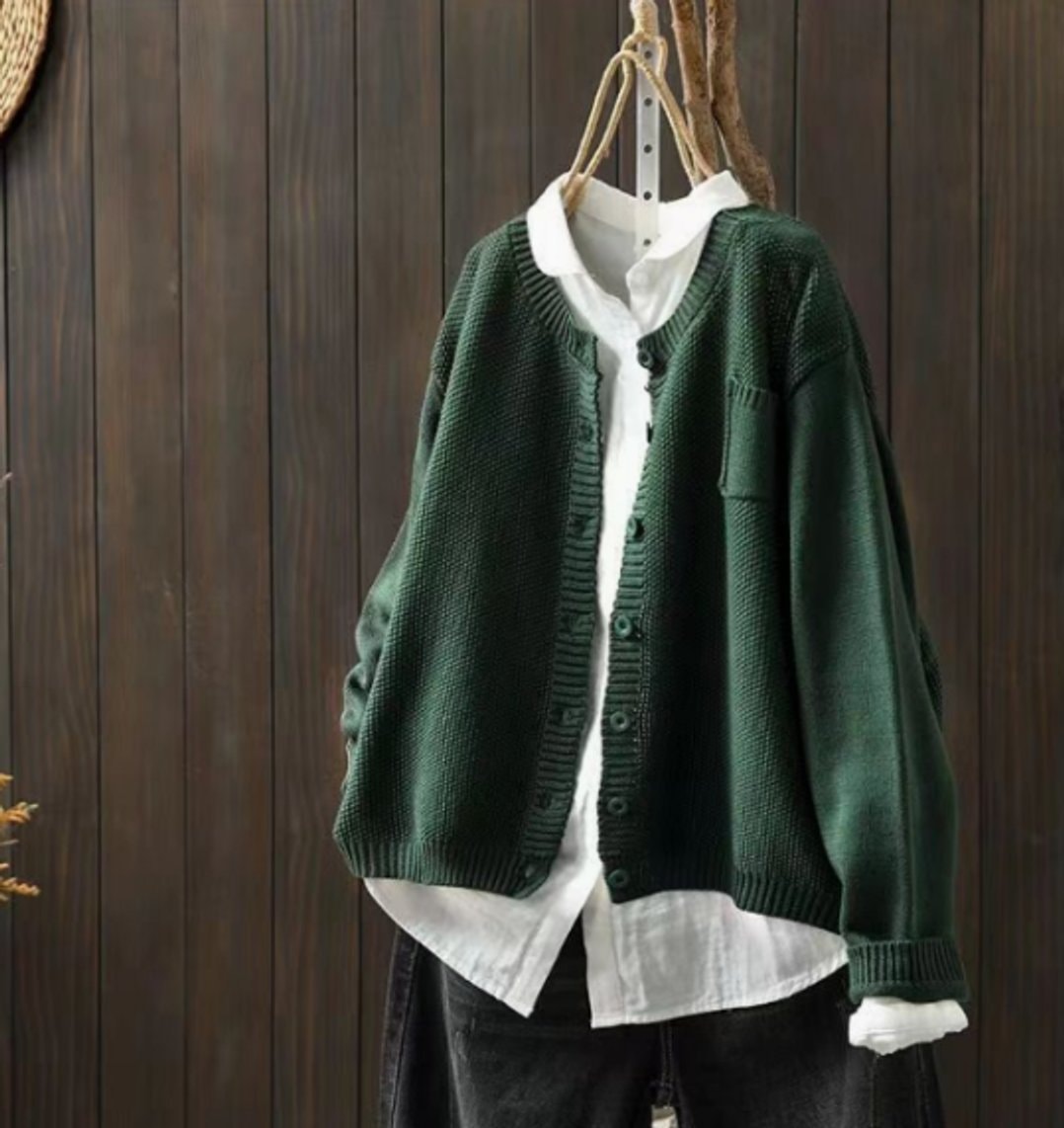 Cárdigan verde oscuro de corte relajado, mostrado abierto sobre una camisa blanca, con escote en V, botones y puños acanalados.