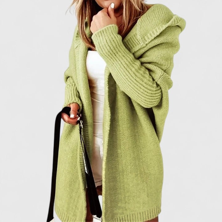 Cárdigan oversize verde claro con capucha, llevado abierto sobre una prenda blanca y acompañado de un bolso negro.
