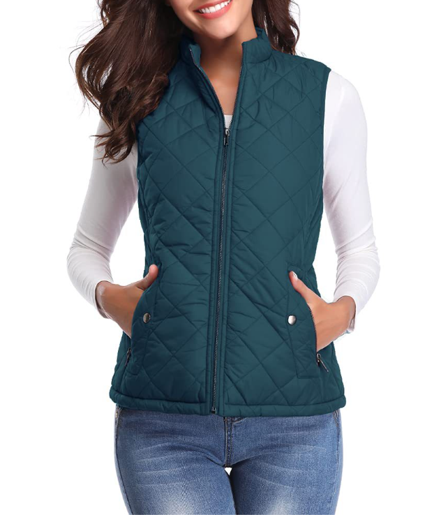 Chaleco acolchado azul petróleo con cuello alto, cierre frontal y bolsillos laterales, combinado con camiseta blanca y vaqueros.