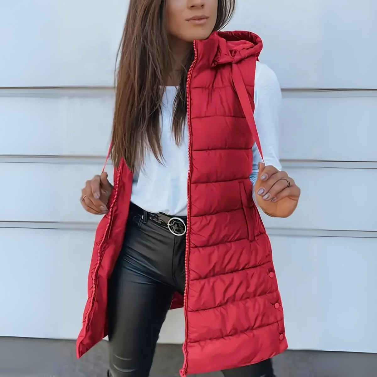 Chaleco acolchado largo rojo con capucha, mostrado abierto mientras la modelo sostiene los laterales.