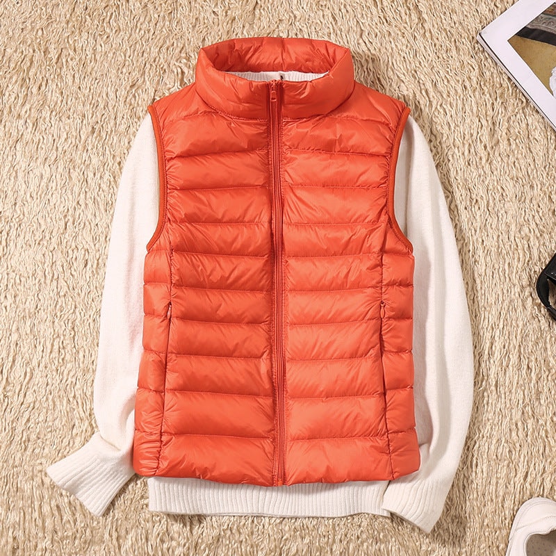 Chaleco acolchado naranja intenso sobre un jersey blanco, con cuello alto y cierre de cremallera frontal.
