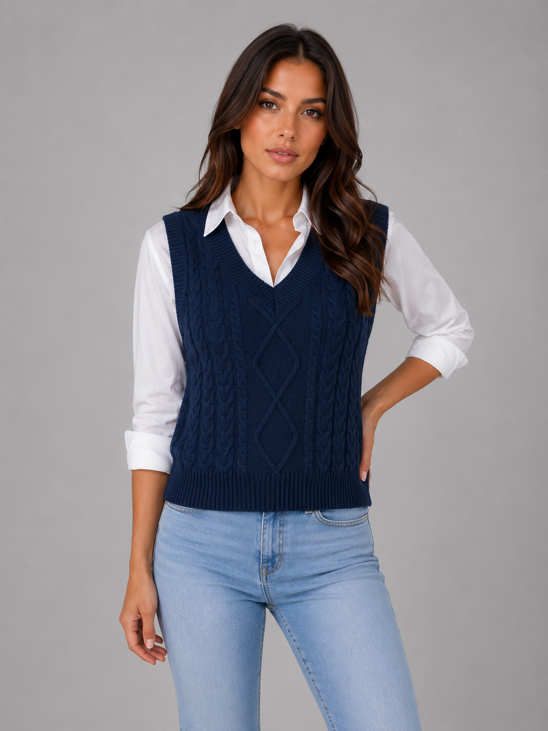 Chaleco azul marino de punto trenzado con cuello en V, combinado con camisa blanca y vaqueros claros.