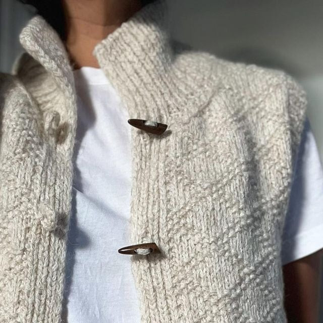 Primer plano frontal del chaleco sobre camiseta blanca, centrado en el cuello levantado y los dos alamares superiores.