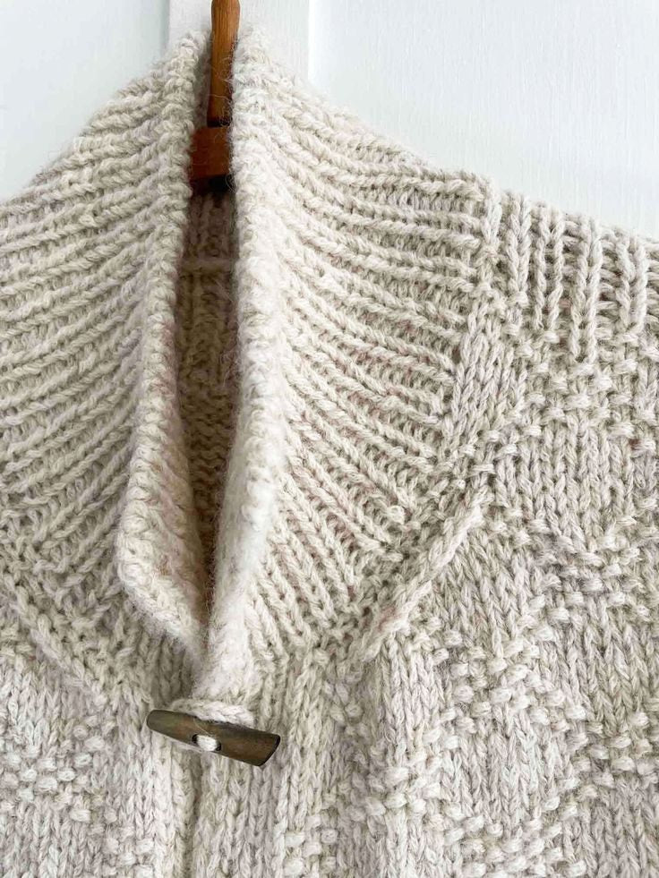 Detalle del cuello alto abierto y del alamar superior, con el patrón de punto visible en el delantero.