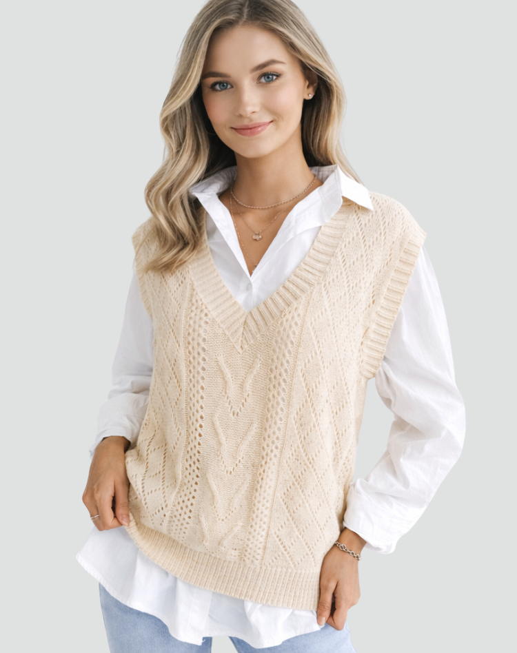 Vista frontal de un chaleco de punto trenzado color crema con escote en V, combinado con camisa blanca y vaqueros claros.