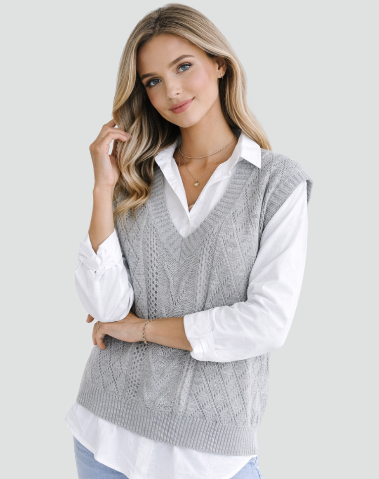 Chaleco gris de punto con textura trenzada y escote en V, mostrado en una pose frontal ligeramente ladeada sobre camisa blanca.