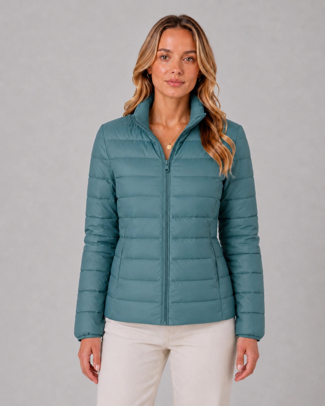 Vista frontal de chaqueta acolchada azul verdosa con cuello alto y cierre completamente cerrado.