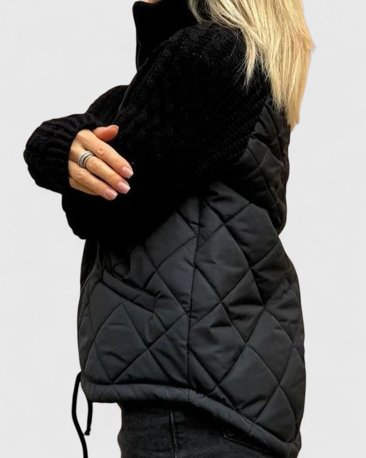 Vista lateral de la chaqueta negra que muestra el cuerpo acolchado, la manga de punto y el cordón ajustable en el bajo.