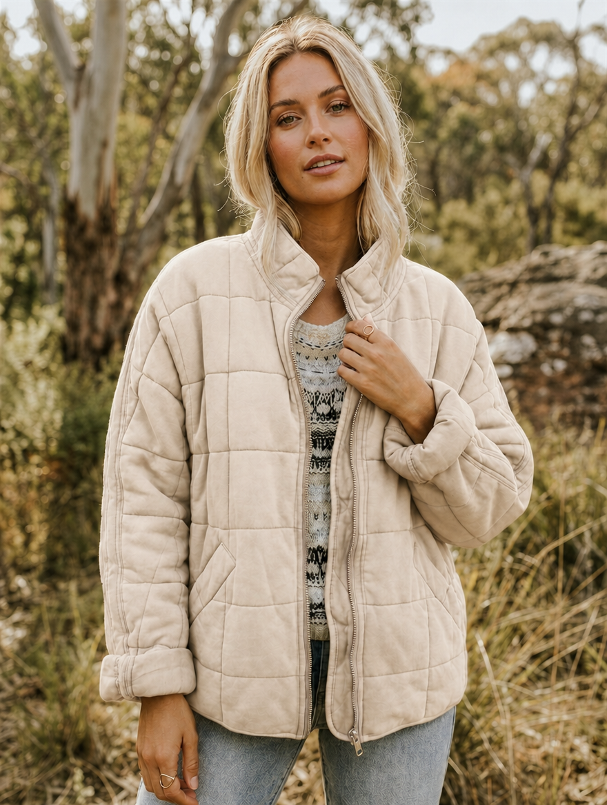 Chaqueta acolchada beige de cuadros con cuello alto, cremallera frontal y bolsillos delanteros, llevada abierta.