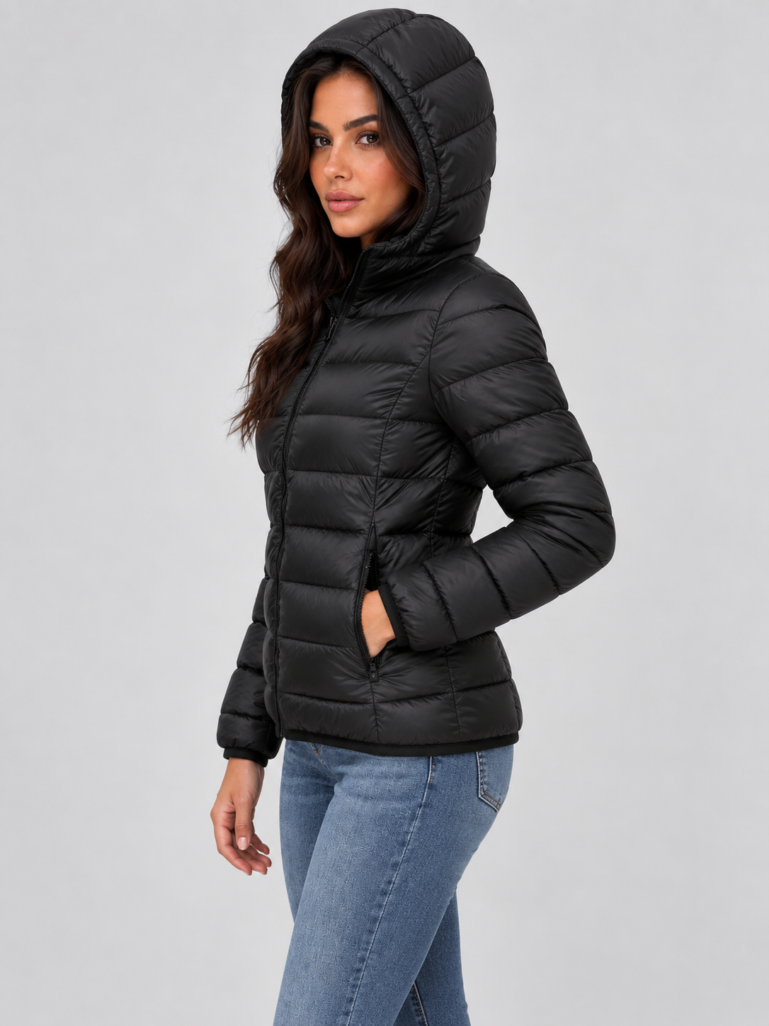 Chaqueta acolchada negra con capucha puesta, mostrada de perfil con una mano en el bolsillo.