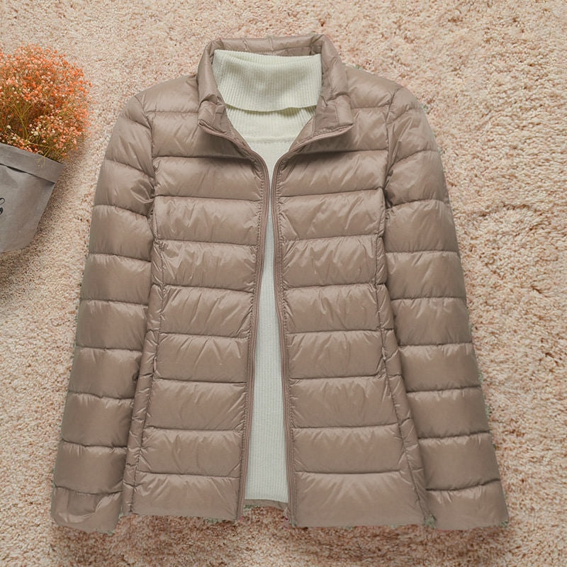 Chaqueta acolchada beige topo con cuello alto y cierre frontal abierto, vista desde arriba.