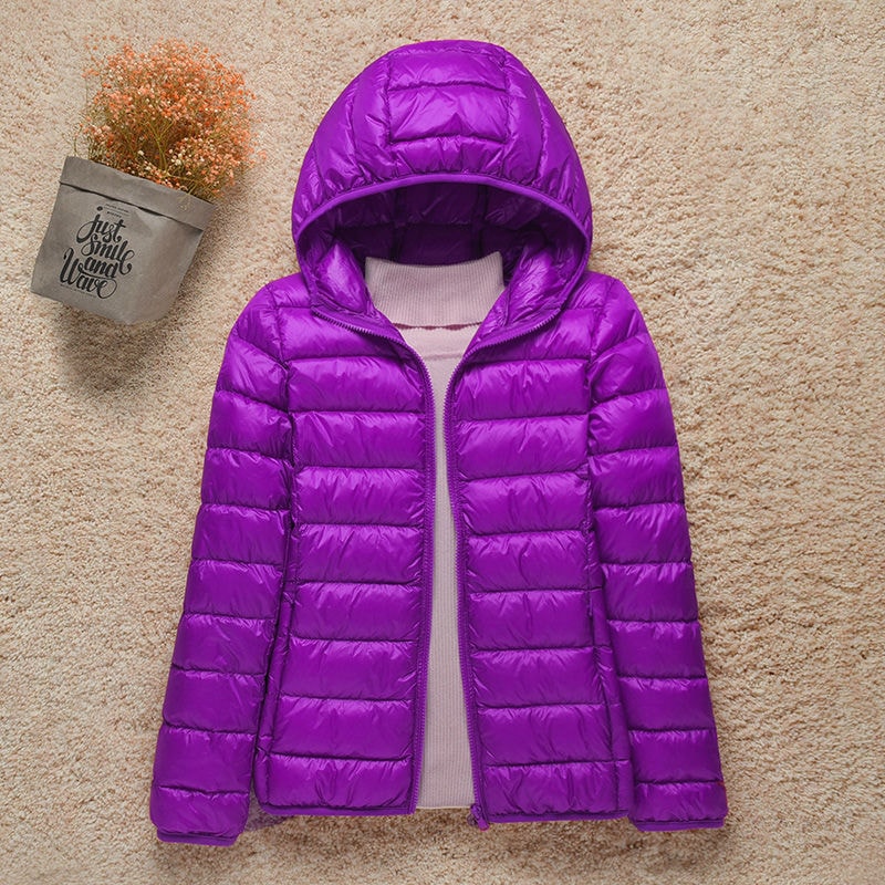 Chaqueta acolchada morada con capucha amplia y cierre frontal visible sobre un jersey claro.