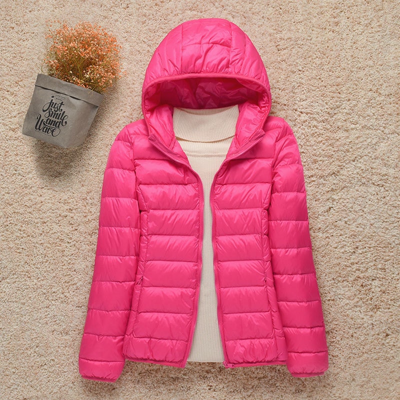 Chaqueta acolchada rosa intenso con capucha y mangas largas, extendida sobre una superficie beige.