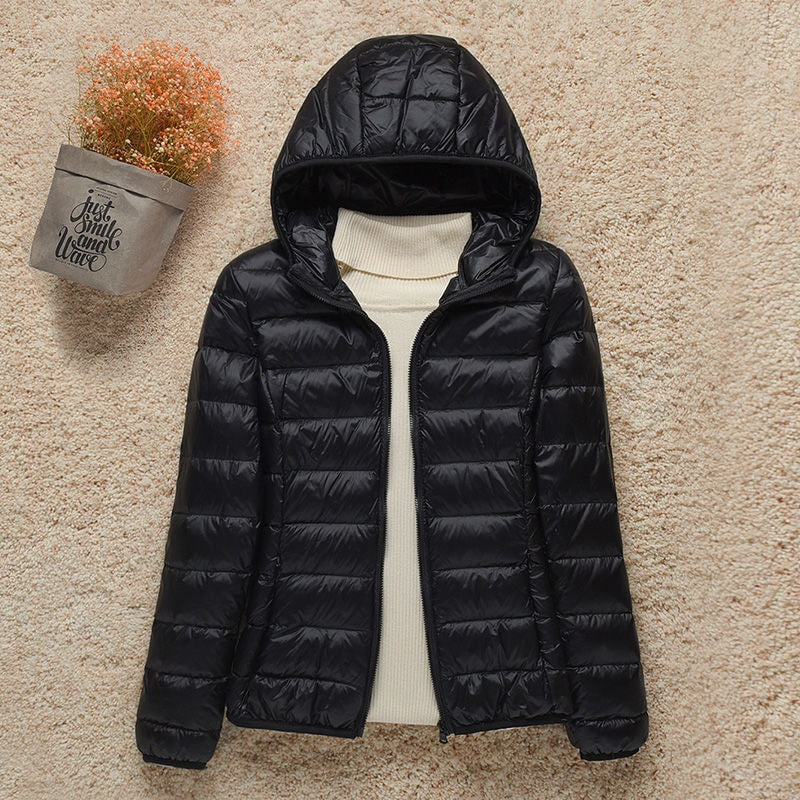 Chaqueta acolchada negra con capucha y acabado brillante, mostrada abierta sobre un jersey de cuello alto.
