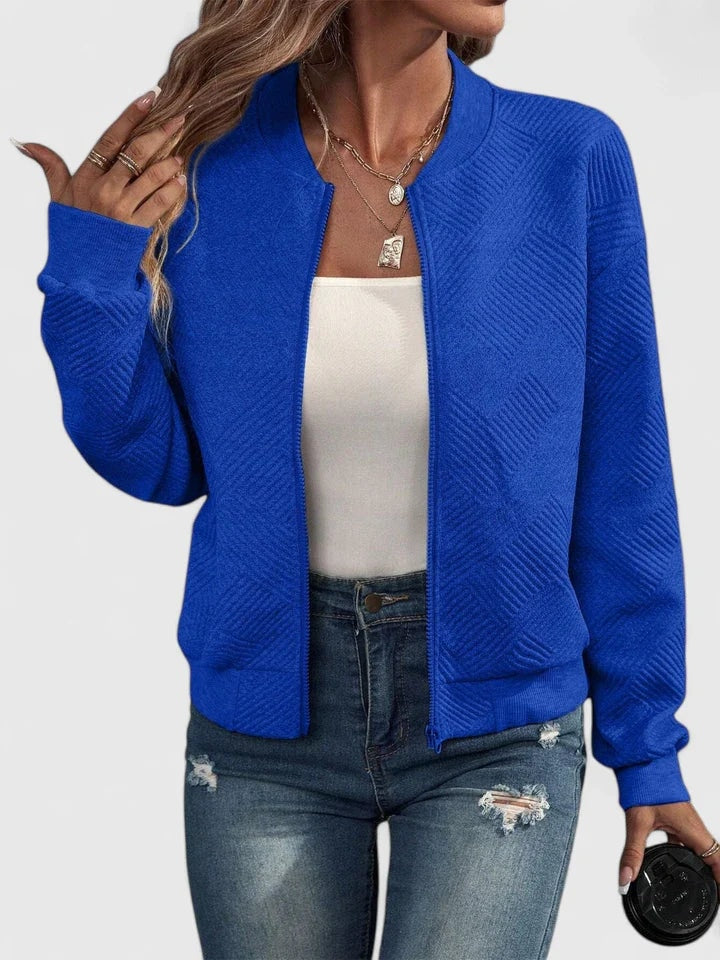 Chaqueta bomber azul intenso con textura geométrica visible en el cuerpo y las mangas, llevada abierta sobre una camiseta clara.