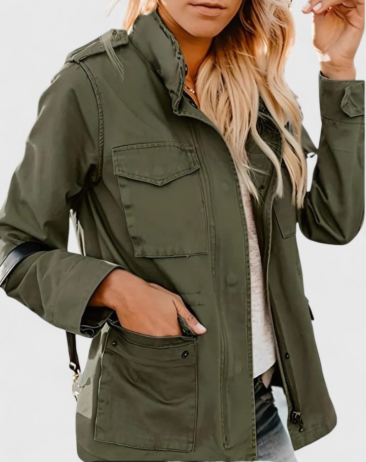 Chaqueta casual verde oliva con cuello alto, cierre delantero y amplios bolsillos frontales, mostrada con una mano en el bolsillo.