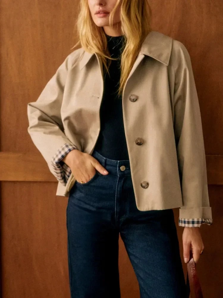 Vista frontal de la chaqueta corta beige con sus tres botones visibles, cuello camisero y puños de cuadros, llevada con una mano en el bolsillo del vaquero.