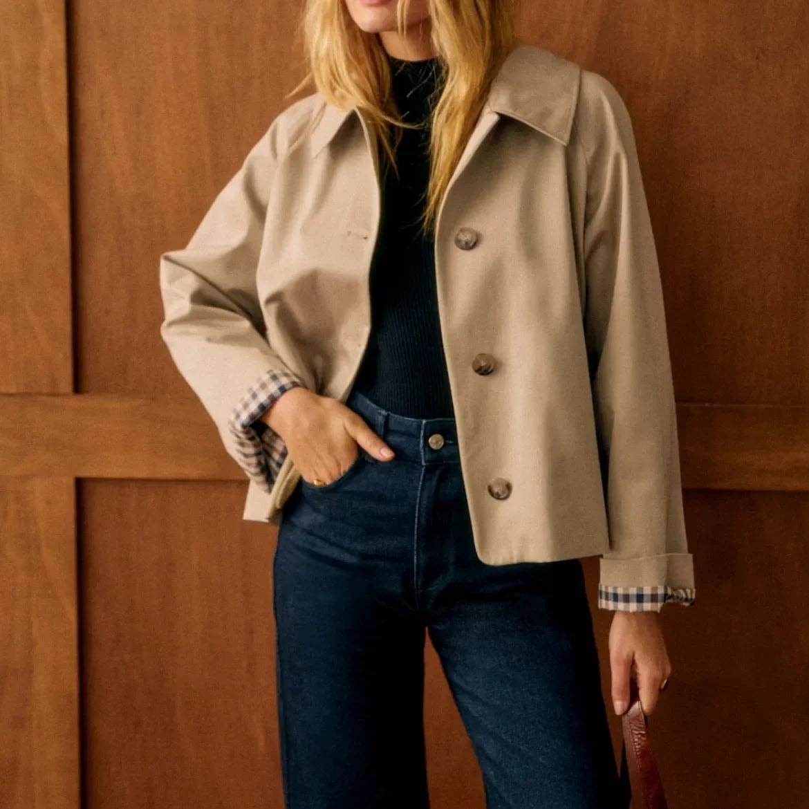 Detalle cercano del frente abotonado de la chaqueta beige, con cuello camisero, puños de cuadros y corte corto sobre vaqueros de tiro alto.