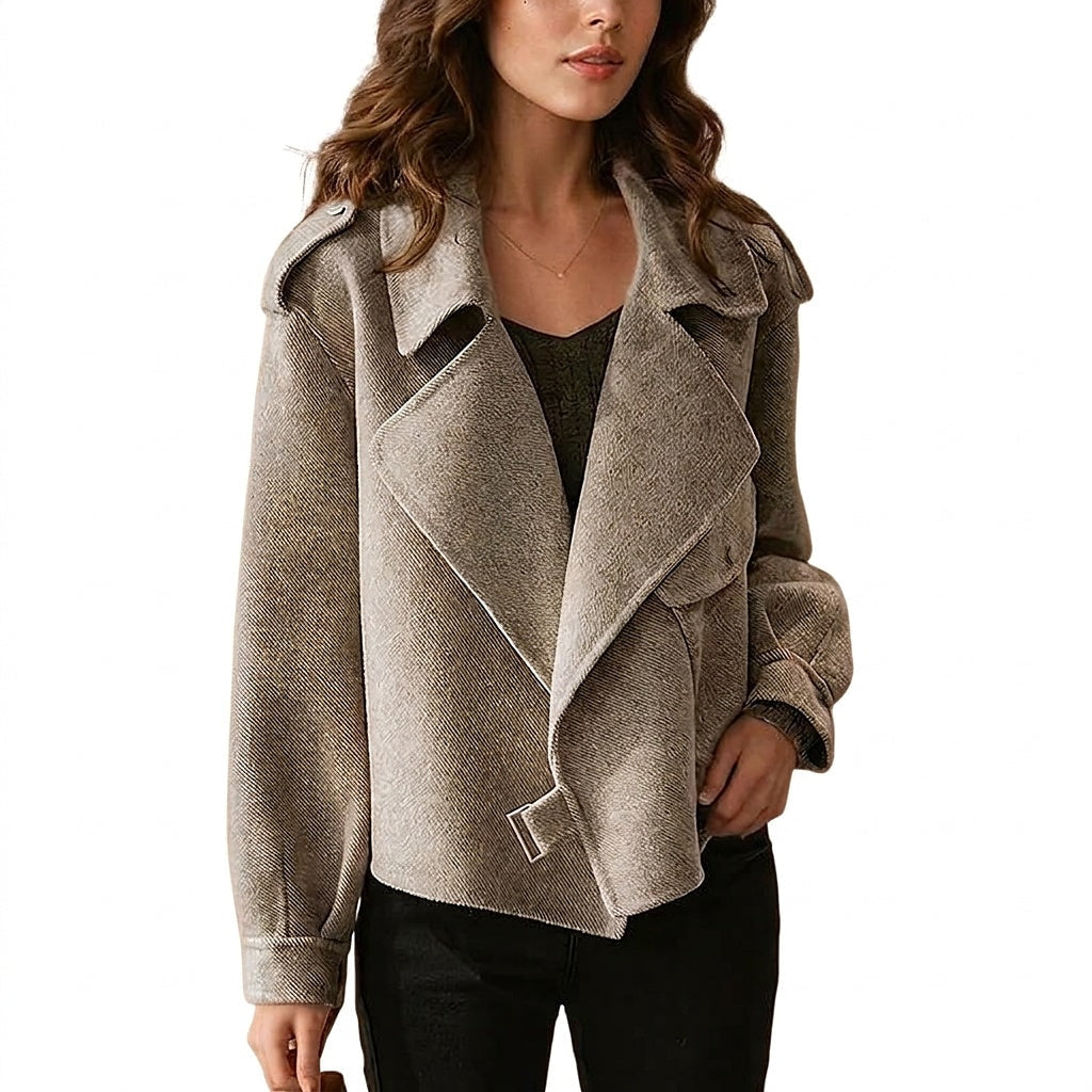 Chaqueta corta de tono beige con solapas amplias, cinturón frontal y detalles en los hombros, combinada con camiseta oscura y pantalón negro.