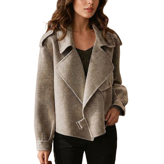 Chaqueta corta de tono beige con solapas amplias, cinturón frontal y detalles en los hombros, combinada con camiseta oscura y pantalón negro.