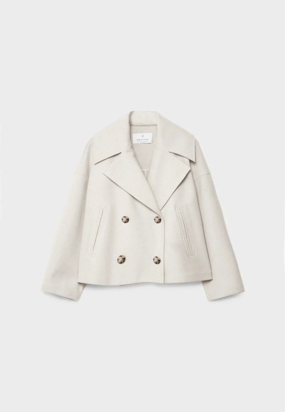Chaqueta corta cruzada en tono marfil, con solapas amplias, cuatro botones y bolsillos verticales.