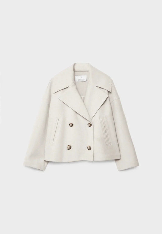 Chaqueta corta cruzada en tono marfil, con solapas amplias, cuatro botones y bolsillos verticales.