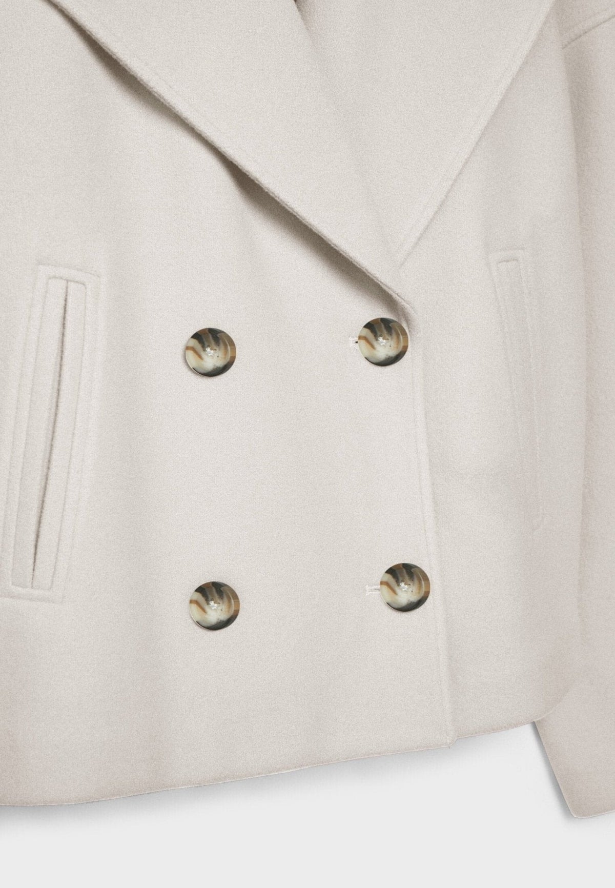 Detalle frontal de la chaqueta marfil con cuatro botones jaspeados, solapa amplia y bolsillo vertical.