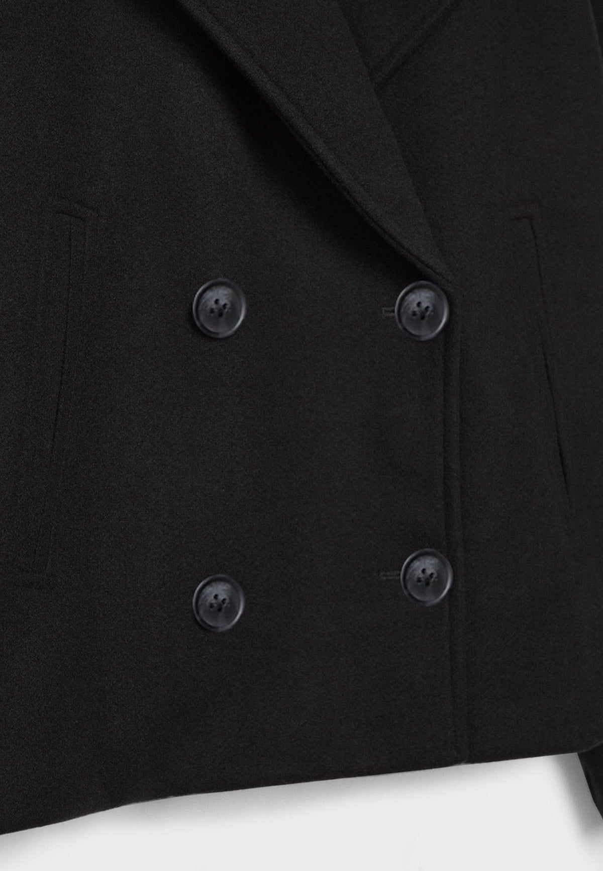 Detalle frontal de la chaqueta negra con cuatro botones oscuros, solapa cruzada y bolsillo lateral.