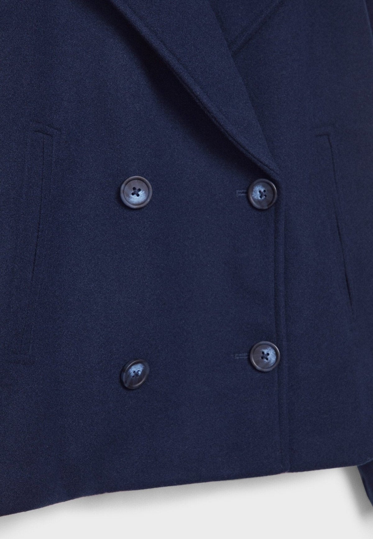 Detalle frontal de la chaqueta azul marino con cuatro botones, solapa cruzada y bolsillo lateral.