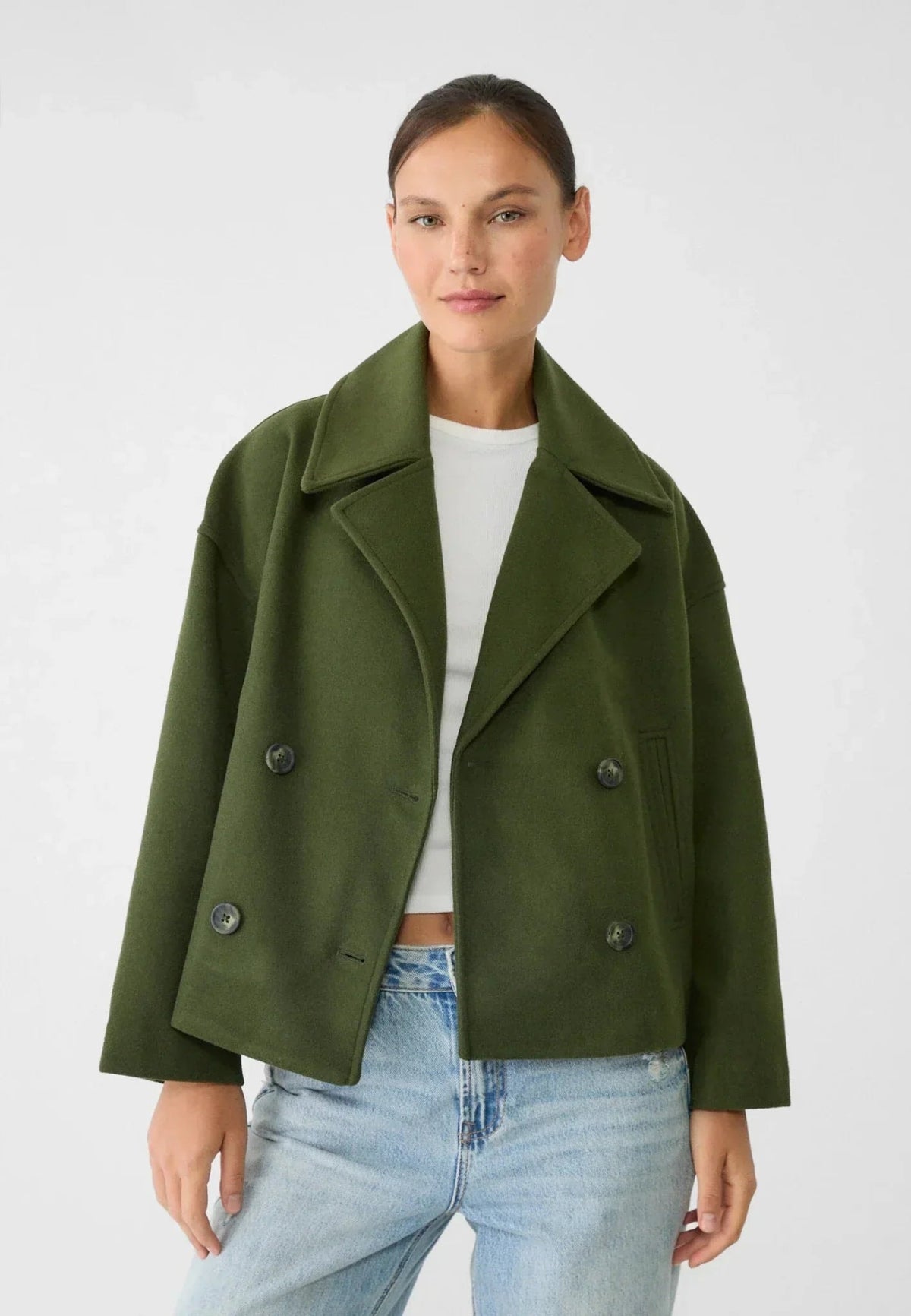 Modelo con chaqueta corta verde oliva sobre una camiseta clara y vaqueros.