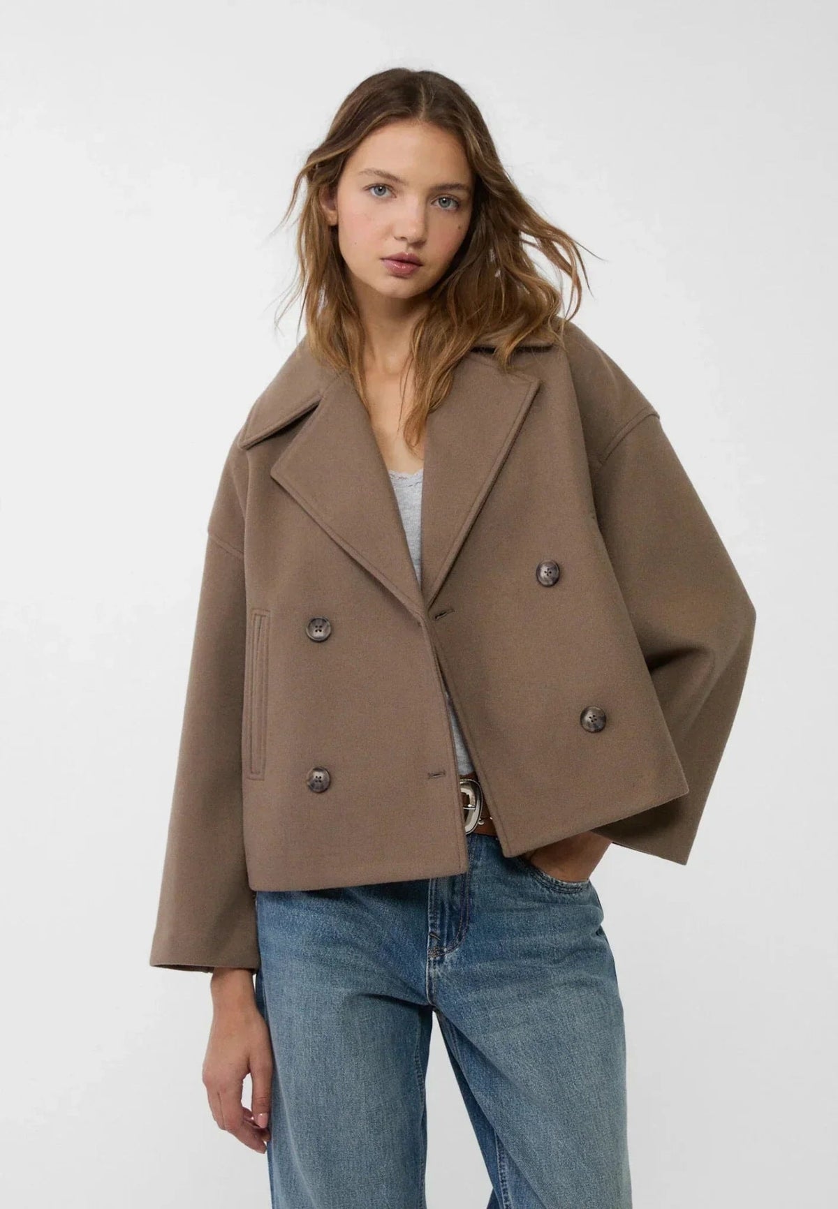 Modelo llevando la chaqueta corta marrón con un lado cruzado sobre el otro y un bolsillo lateral visible.