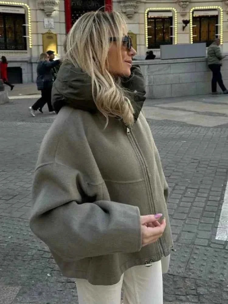 Chaqueta oversize en tono gris verdoso, vista de perfil, con cuello acolchado envolvente y cierre frontal.