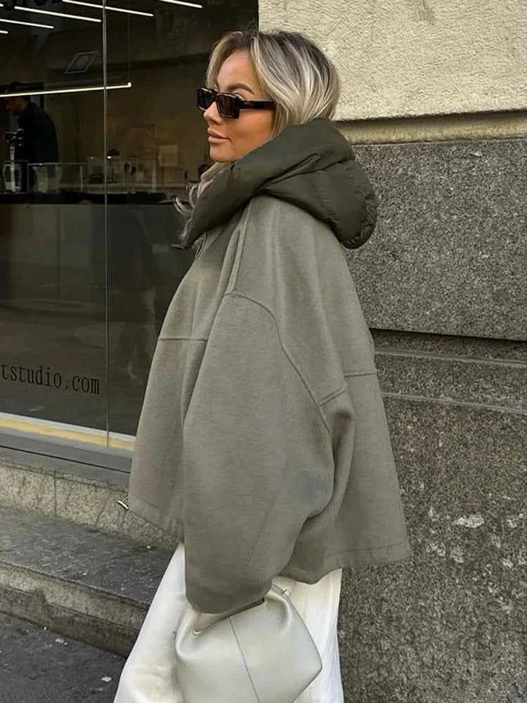 Chaqueta oversize vista de lado junto a un escaparate, combinada con pantalón claro y cuello acolchado prominente.