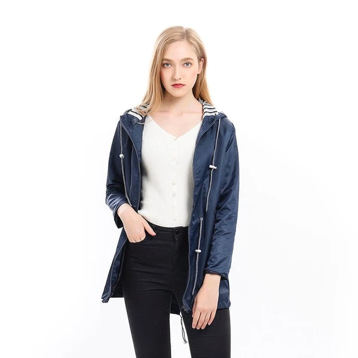 Mujer con chubasquero ligero azul marino, capucha abierta y cordones ajustables, combinado con pantalones negros.