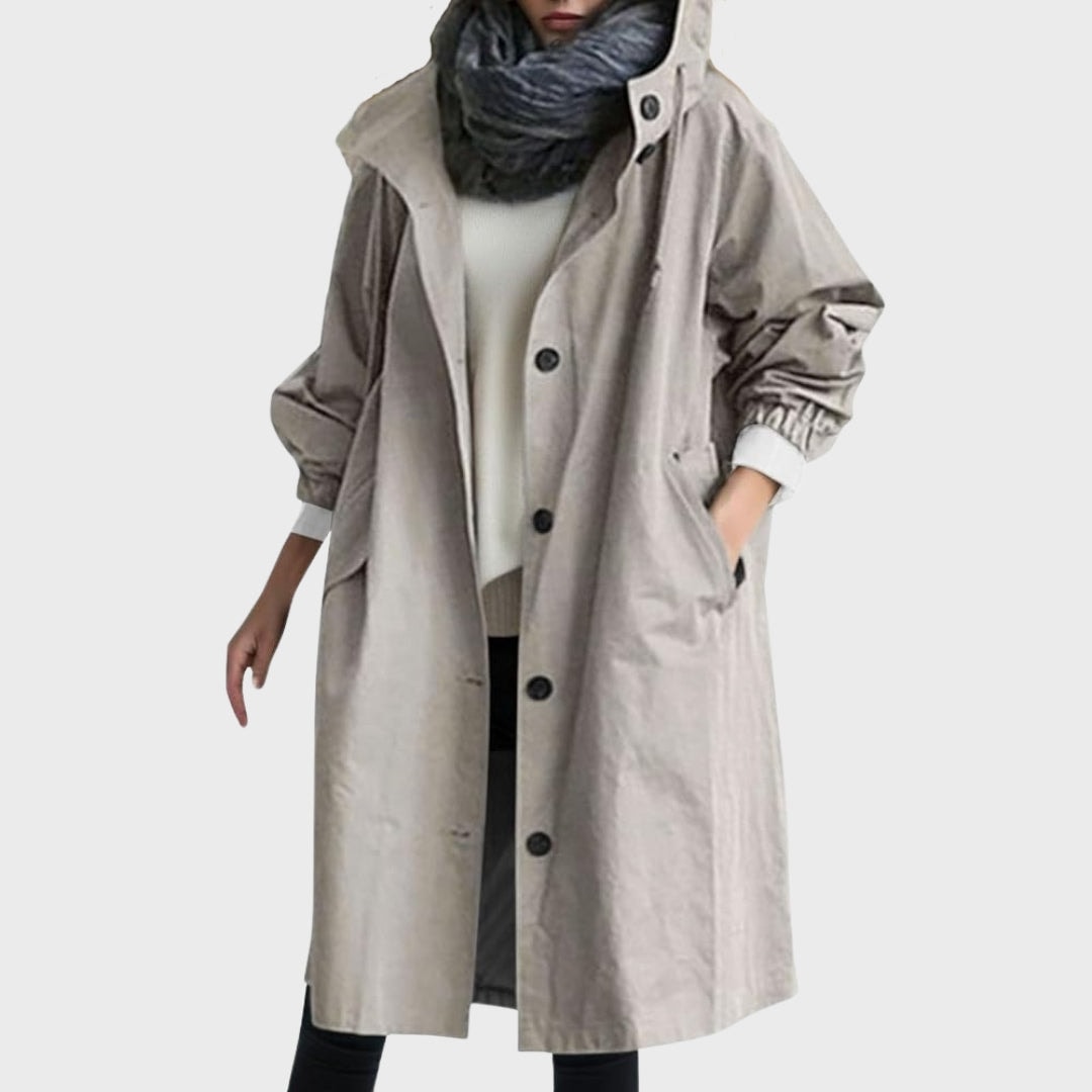 Gabardina larga gris claro con capucha, cierre frontal de botones, bolsillos laterales y puños elásticos.